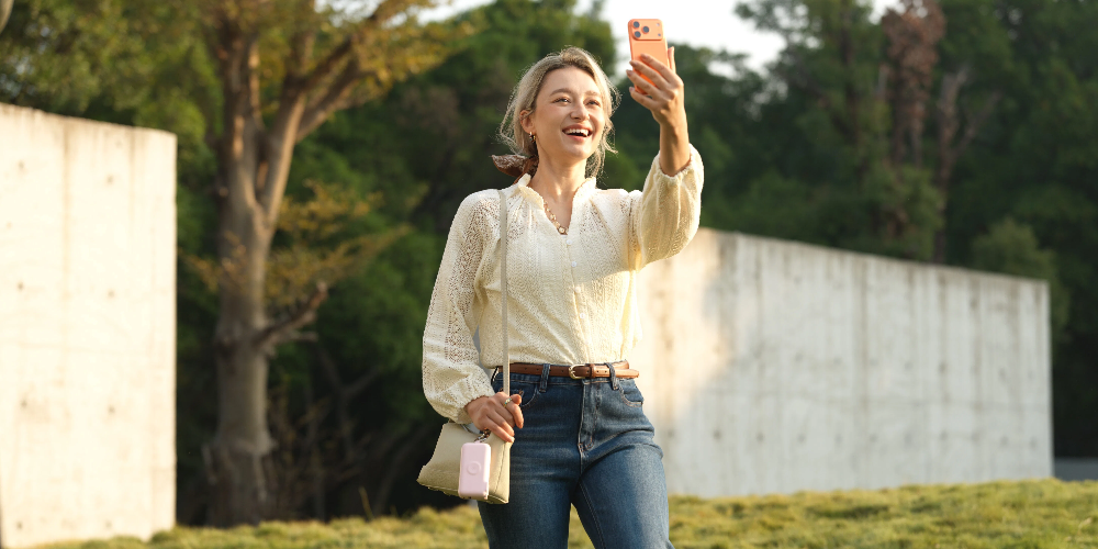 `Happy woman outdoors taking selfie with smartphone, carrying RORRY CB4-10000mAh portable power bank in pastel pink