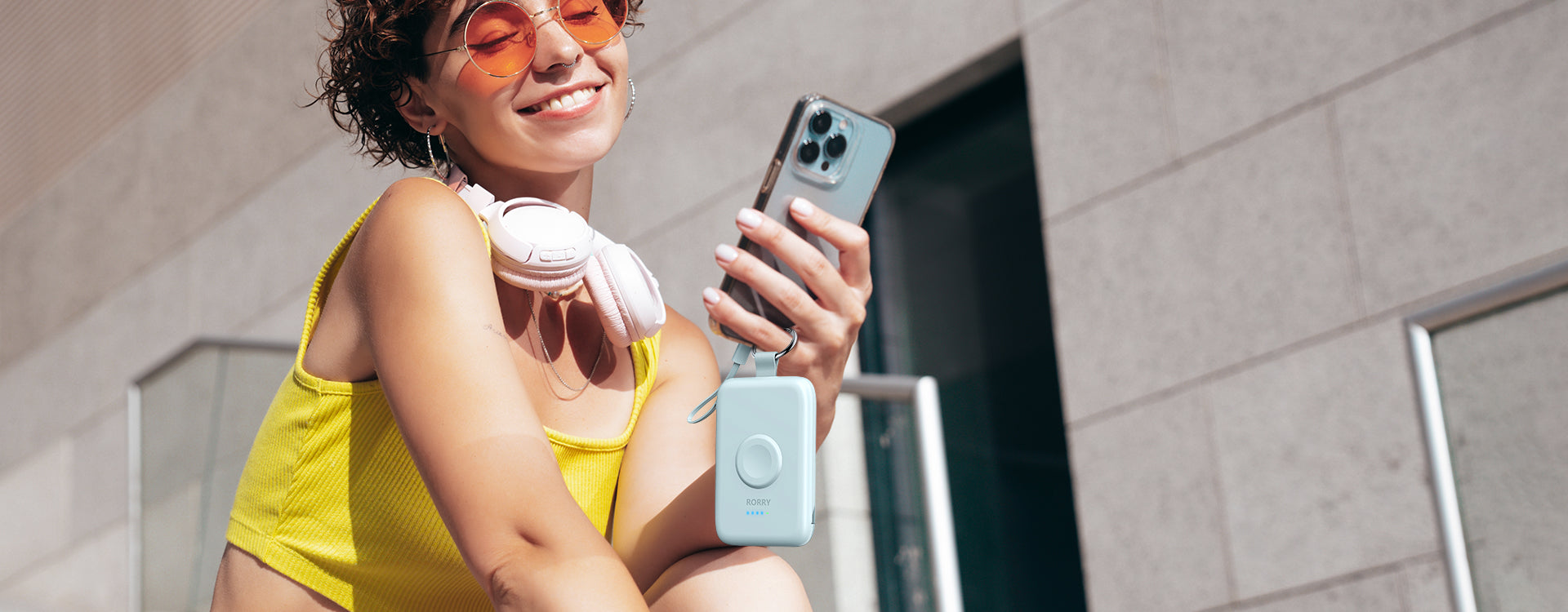 A smiling modern woman using RORRY aesthetic light blue keychain portable charger for her iPhone outdoors, showcasing stylish and cable-free charging lifestyle.